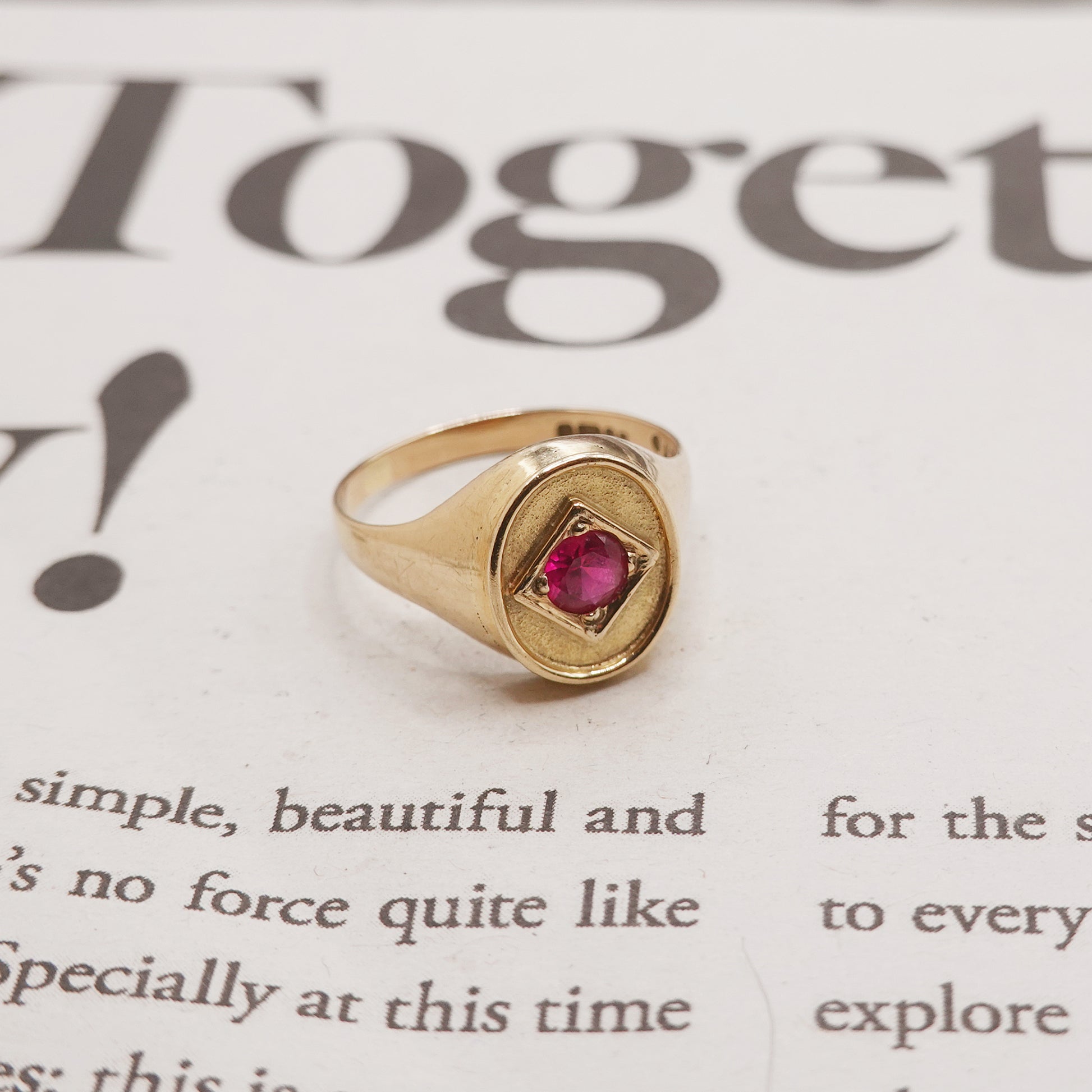 Gold ring with a red gemstone on a piece of paper with text.