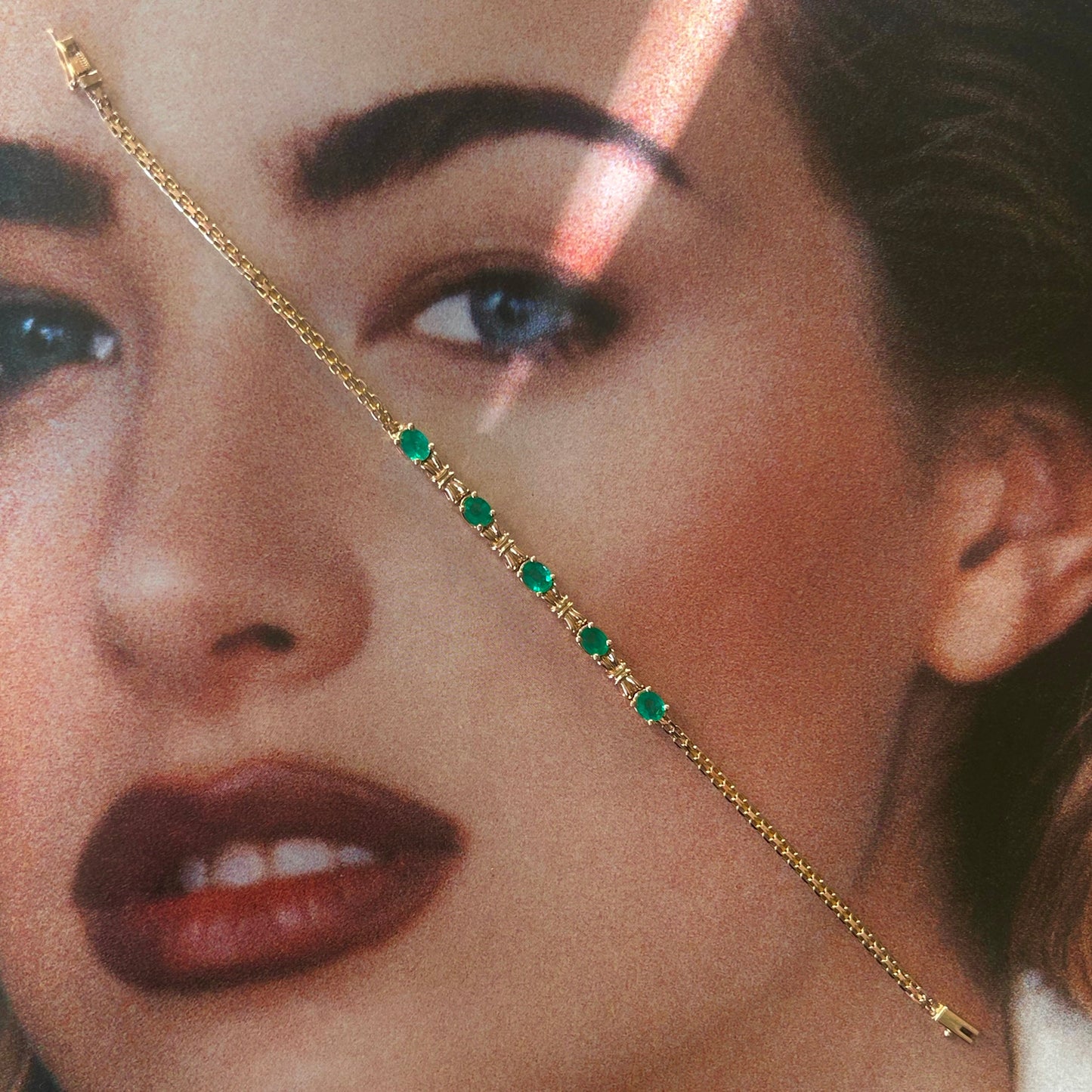 Close-up of a woman's face wearing a gold chain with green gemstones.