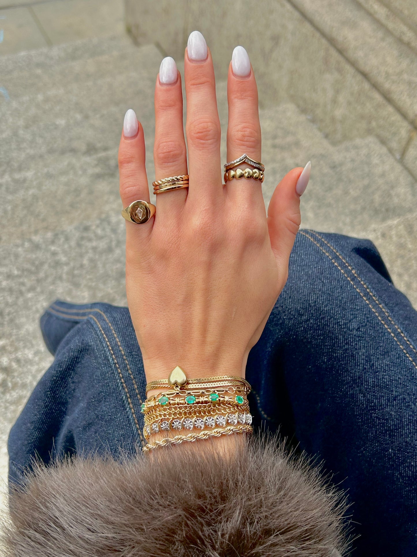 Hand wearing multiple gold rings and bracelets with a blurred background