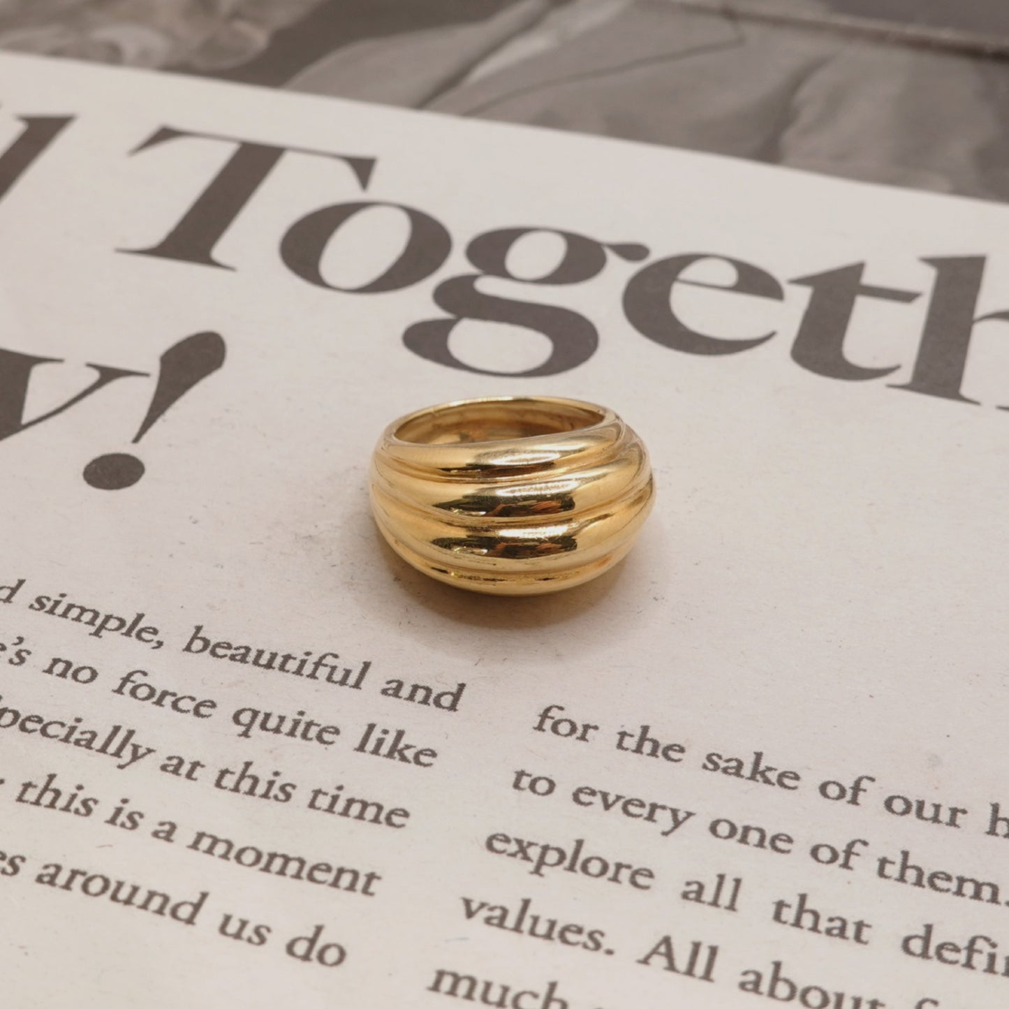 A gold-colored multi-band ring with a polished, ribbed design, resting on a printed book page.