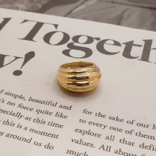 A gold-colored multi-band ring with a polished, ribbed design, resting on a printed book page.