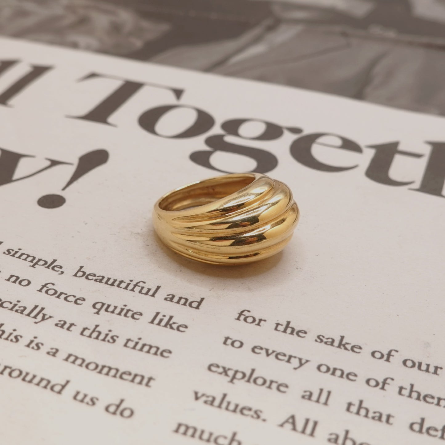 A gold-toned multi-band ring with a polished finish, resting on a printed book page.