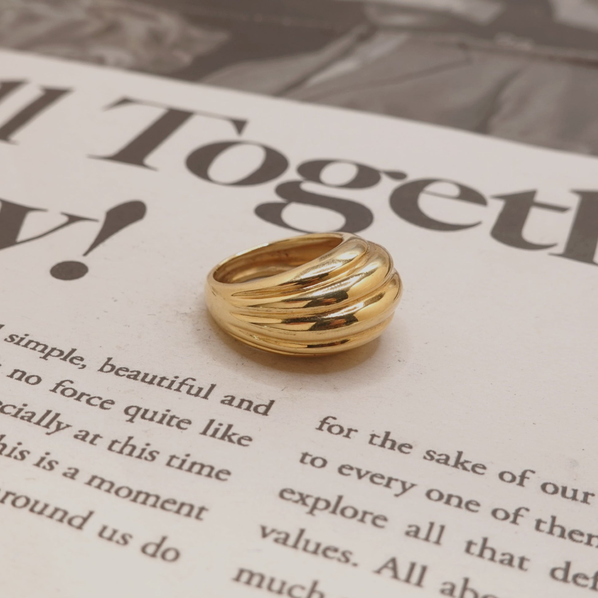 A gold-toned multi-band ring with a polished finish, resting on a printed book page.
