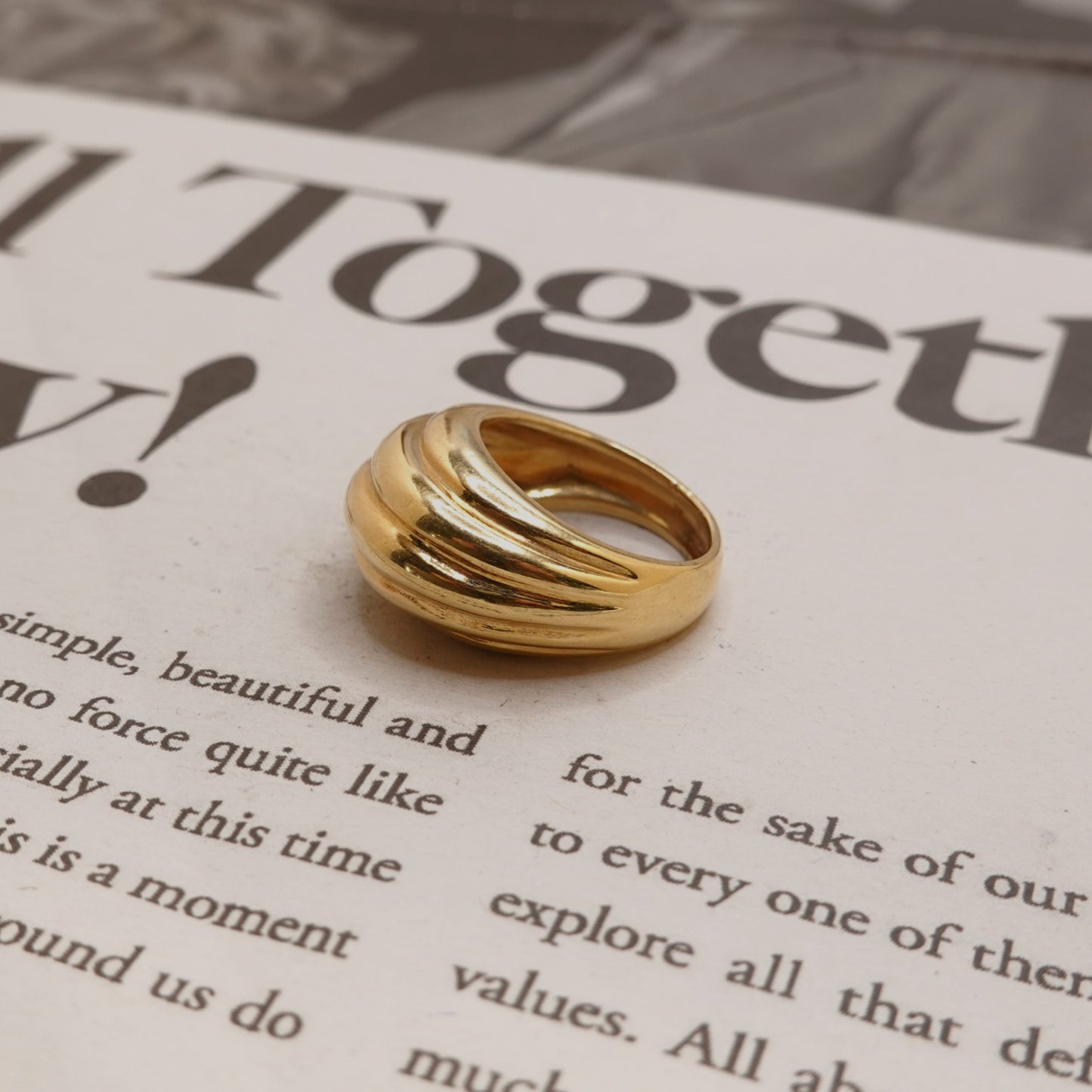 A polished gold ring with three interlocking curved bands, resting on an open book page with printed text.