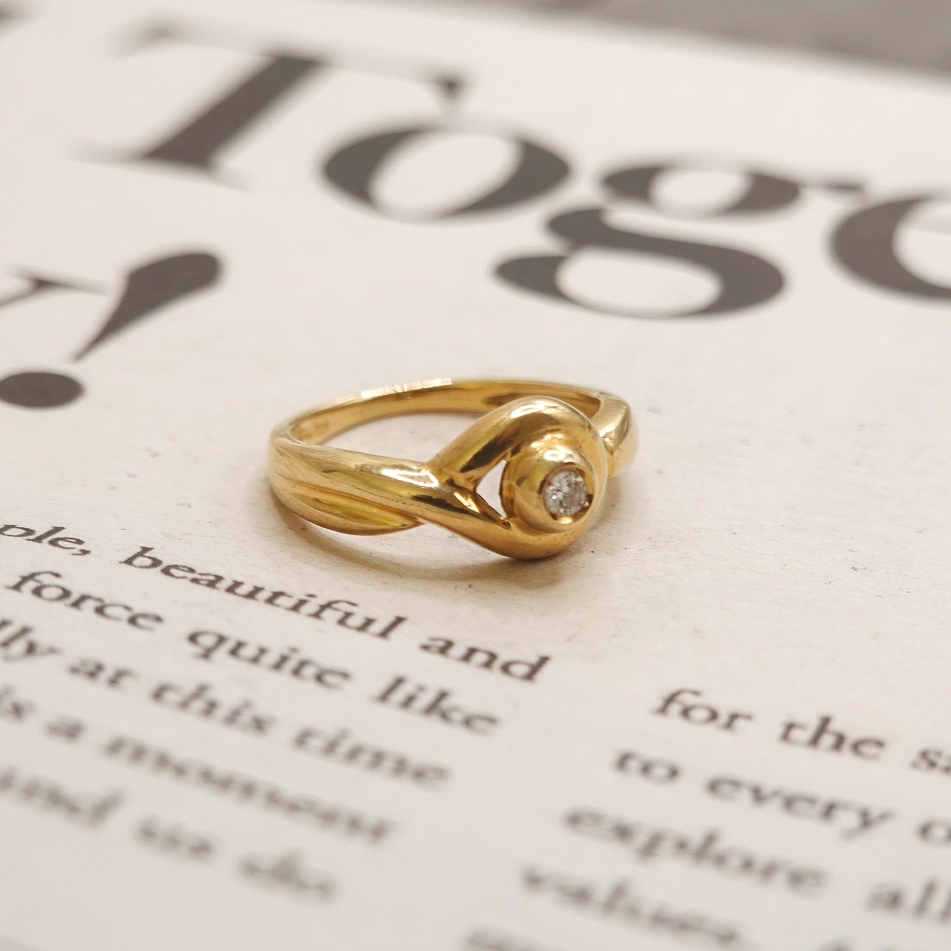 Gold ring with a diamond on a blurred text background