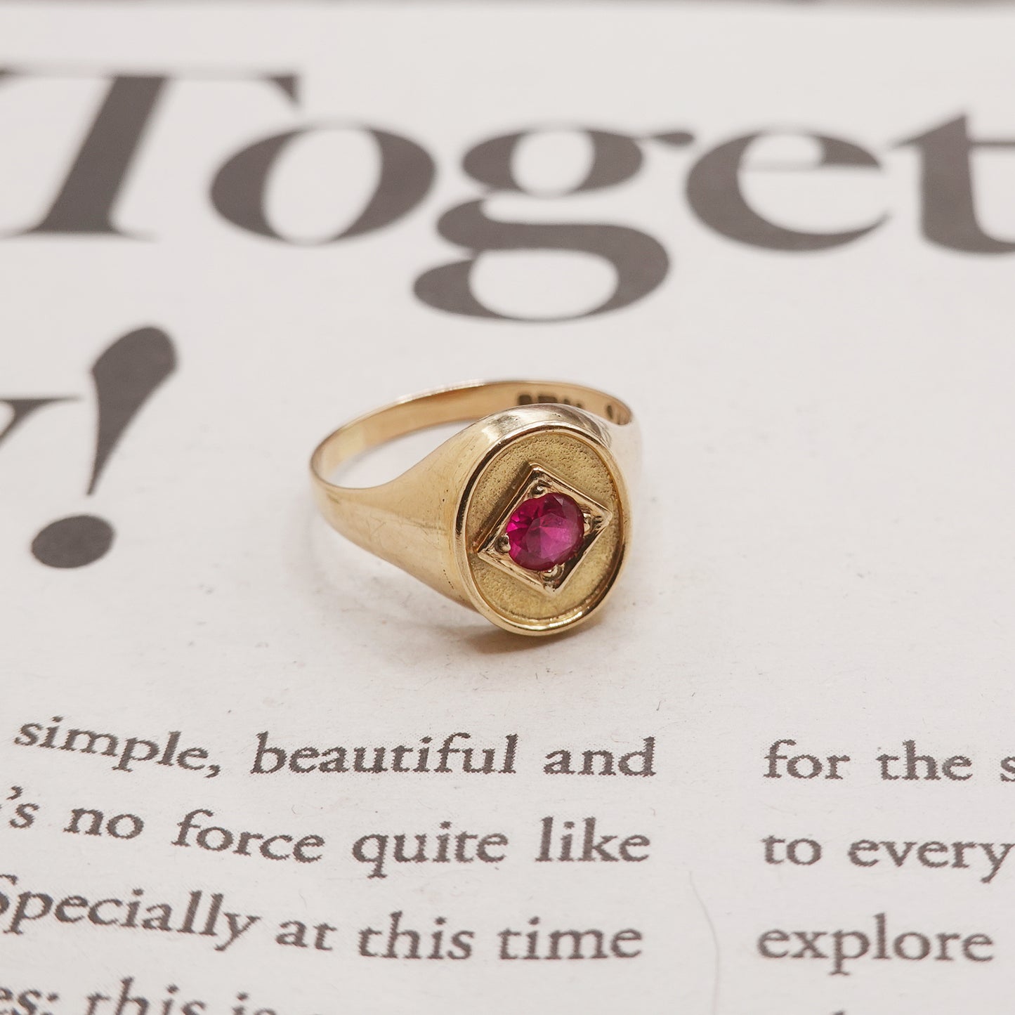 Gold ring with a red gemstone on a piece of paper with text.