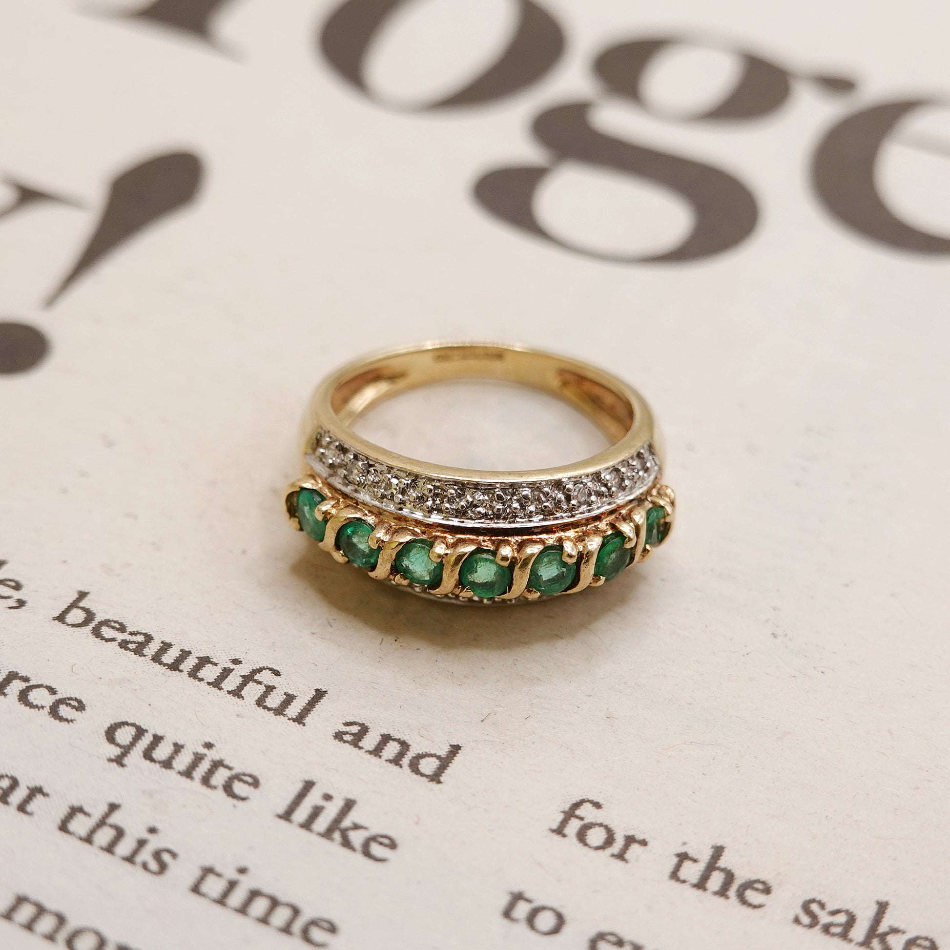 Gold ring with green green emerald and diamonds on a piece of paper