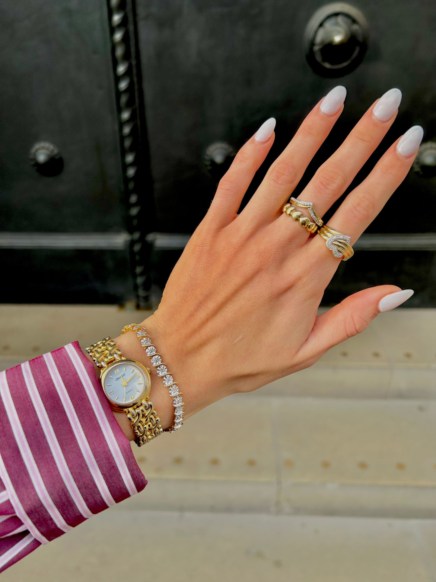Hand with gold watch, bracelets, and rings against a blurred background