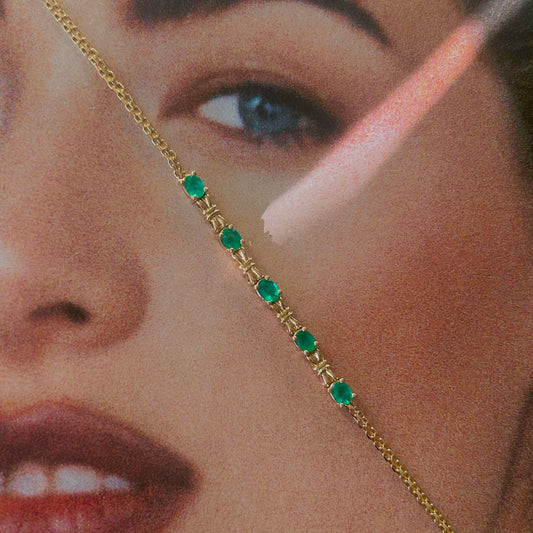 Close-up of a face wearing a gold chain with green gemstones.