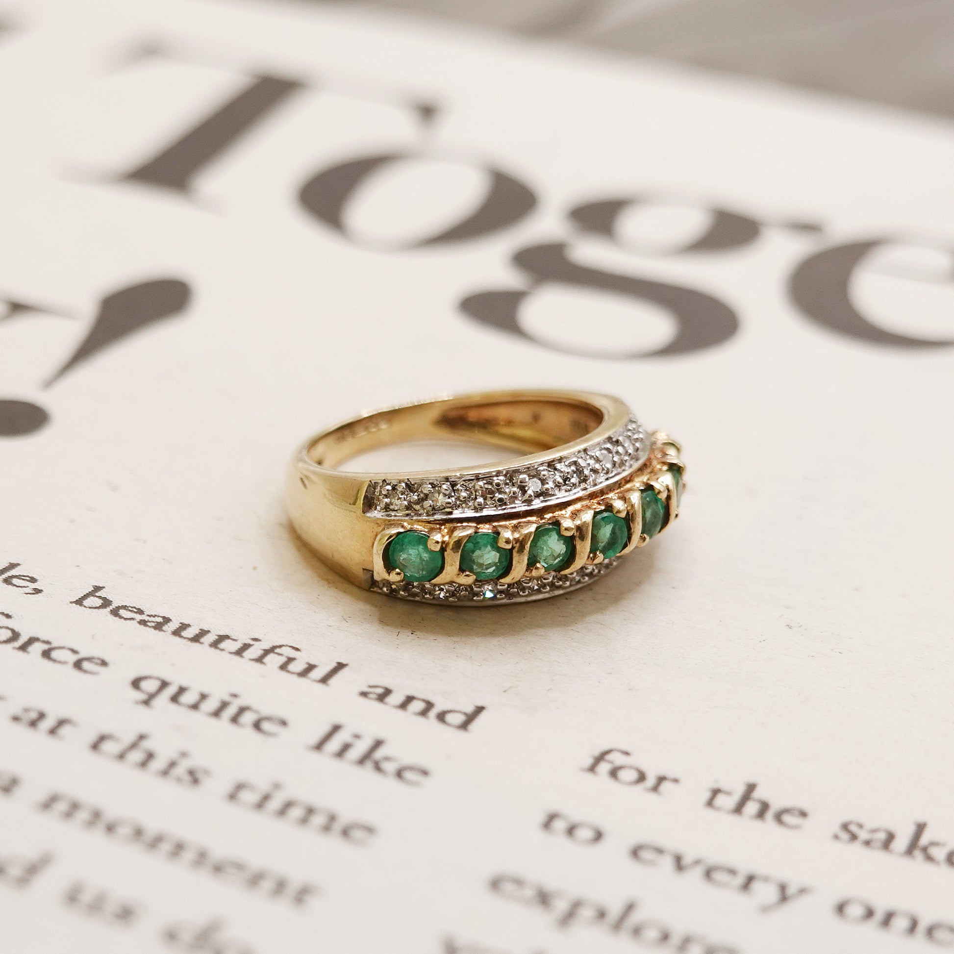 Gold ring with green emerald and diamonds on a magazine page